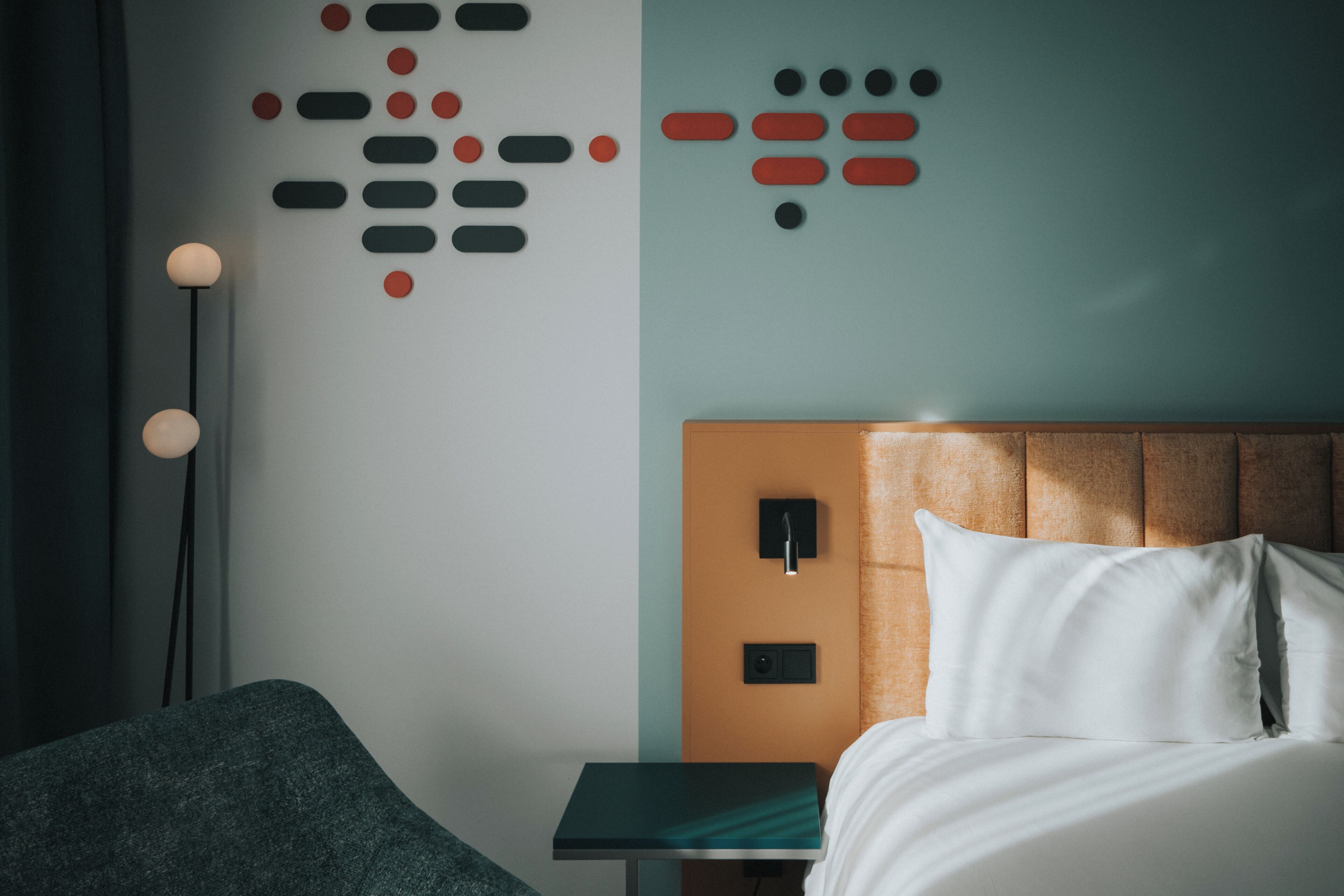 A modern hotel room with a bed, a nightstand, a wall art installation, and a floor lamp.
