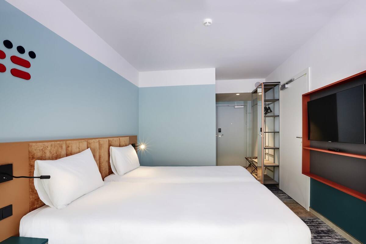 A hotel room with a large bed, a TV mounted on the wall, and a wardrobe.