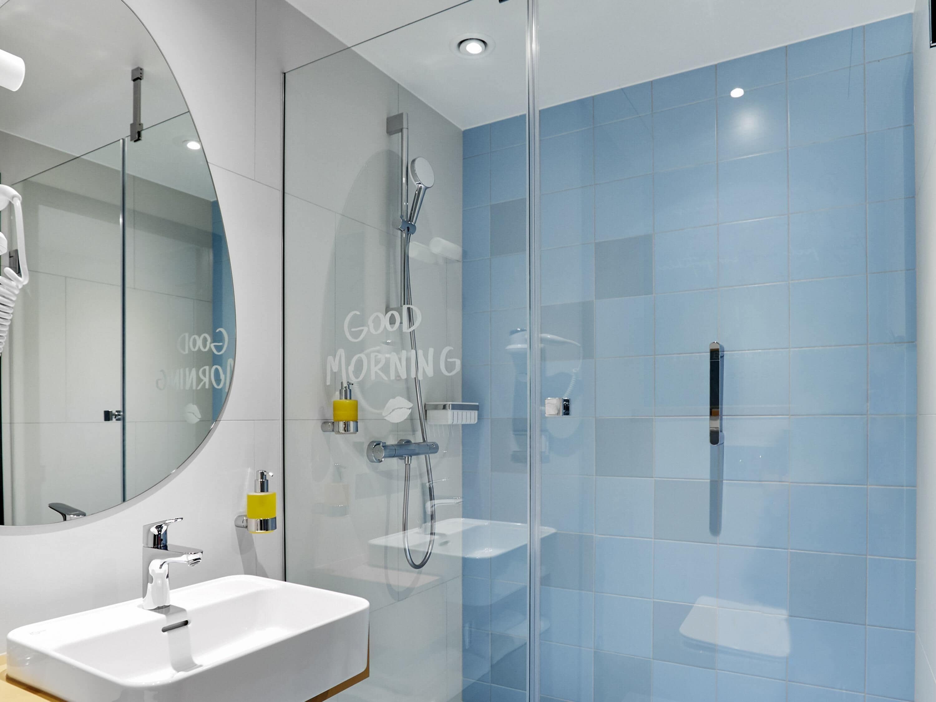 Une salle de bain moderne avec un lavabo blanc, une cabine de douche en verre et un mur recouvert de carreaux bleus.