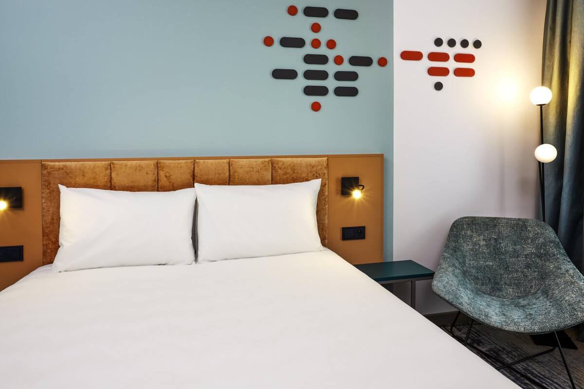 A hotel room with a bed, a chair, and wall art.