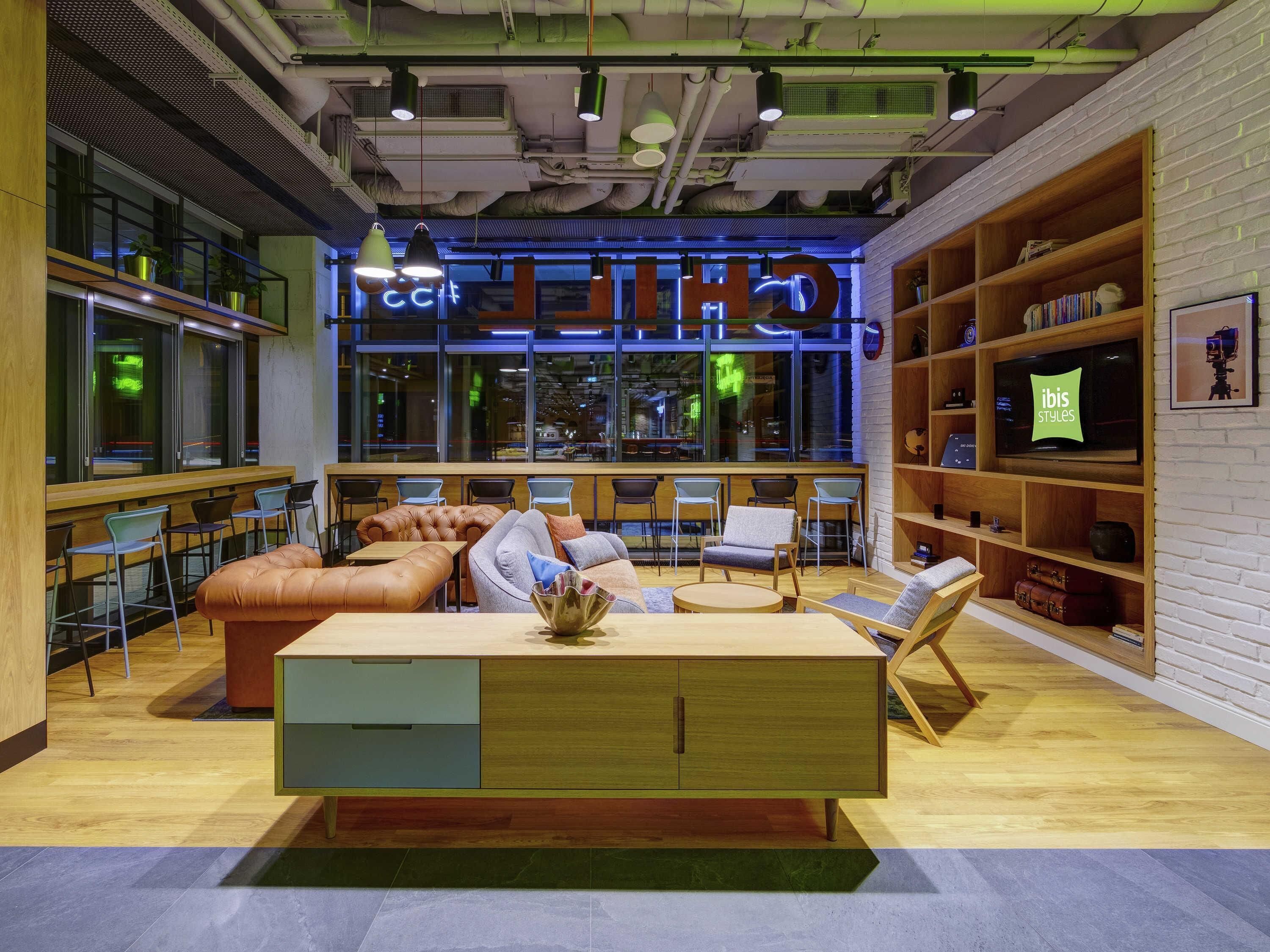 A modern lounge area with seating, a wooden coffee table, and a television displaying 'ibis Styles'.