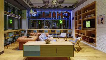 A modern lounge area with seating, a wooden coffee table, and a television displaying 'ibis Styles'.