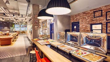 A buffet area with various food options, a seating area with chairs, and a brick wall with framed pictures.