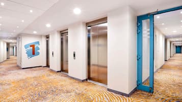 A hotel corridor with elevators, a blue door, and a patterned carpet.
