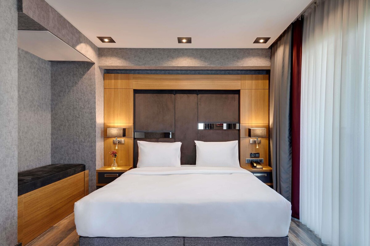A modern hotel room with a large bed, bedside lamps, and a built-in headboard.