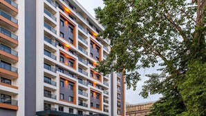 Un hotel de varios pisos con fachada moderna, ventanas amplias y un área exterior bien cuidada con un sendero y vegetación.