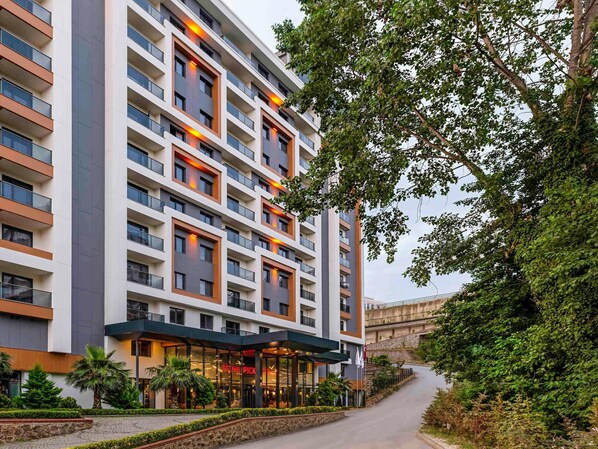A multi-story hotel with a modern facade, large windows, and a well-maintained outdoor area with a pathway and greenery. - Mövenpick Hotel Trabzon (Trabzon)