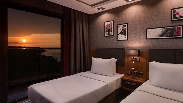 Habitación de hotel con dos camas, un ventanal con vista al atardecer y obras de arte en las paredes.