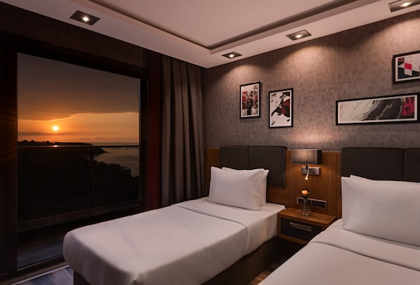 A hotel room with two beds, a large window with a sunset view, and artwork on the walls. - Mövenpick Hotel Trabzon (Trabzon)