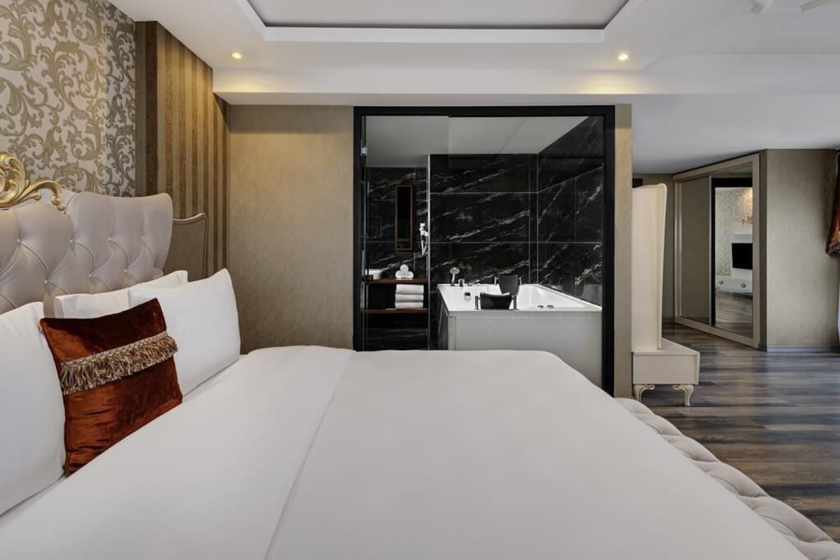 A modern hotel room with a large bed, a bathroom with a marble sink, and a walk-in closet.