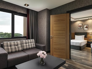 Habitación de hotel moderna con sofá, una mesa de centro con flores, una puerta de madera, una cama y vistas a la ciudad.