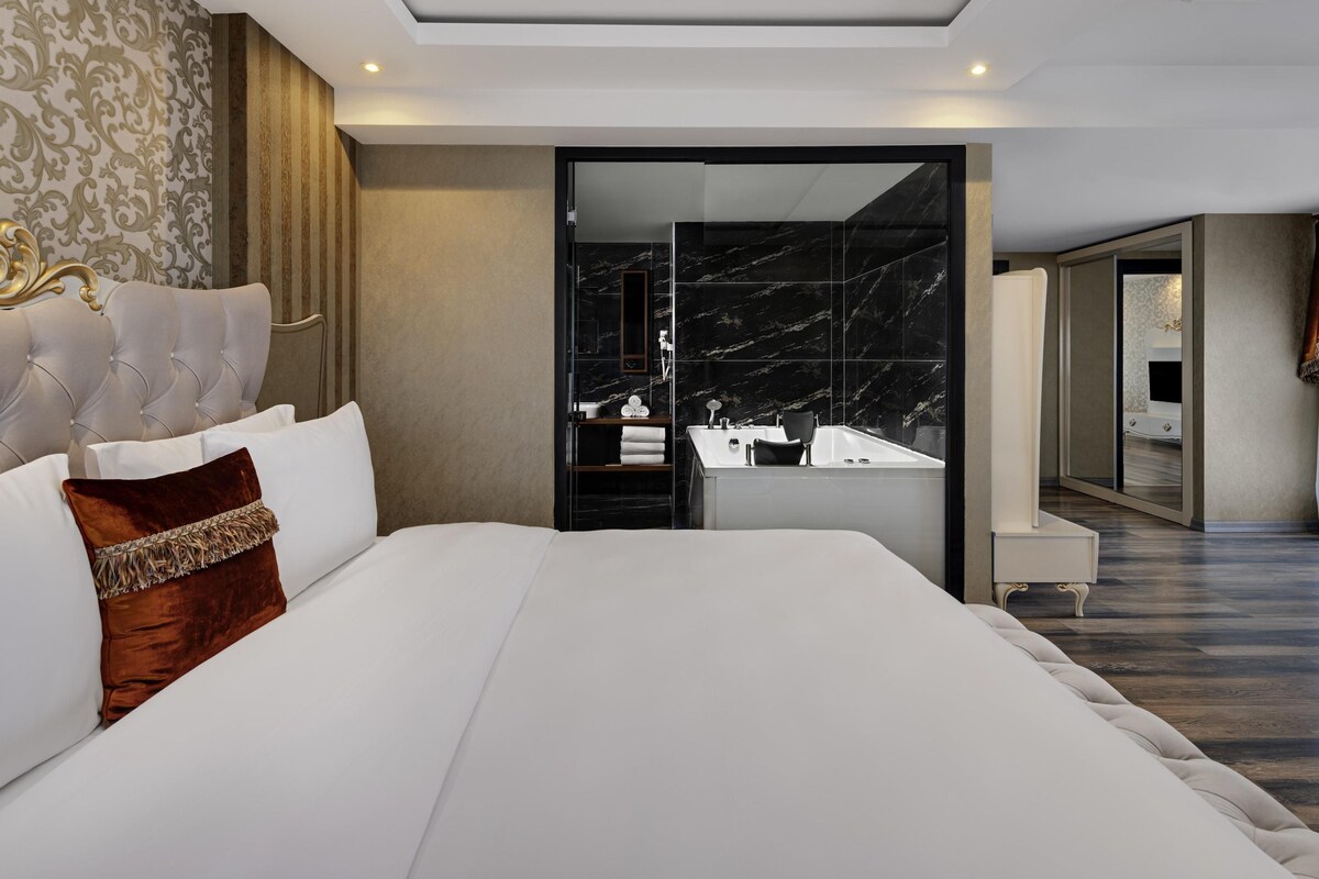 Una habitación de hotel moderna con una cama grande, un baño con lavamanos de mármol y vistas al pasillo.