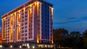Un hotel de varios pisos con un diseño moderno, que destaca por su entrada principal e iluminación frontal.