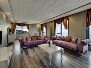 Ein modernes Wohnzimmer mit zwei Sofas, einem Couchtisch und Blick auf eine Stadtlandschaft.