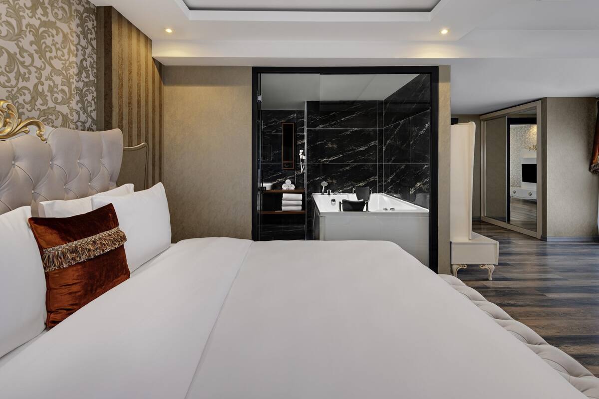 A modern hotel room with a large bed, a bathroom with a marble sink, and a view of the hallway.