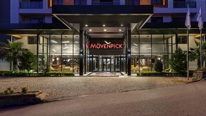 Entrada de hotel con fachada de vidrio, un letrero que dice 'MÖVENPICK' y un vestíbulo bien iluminado.