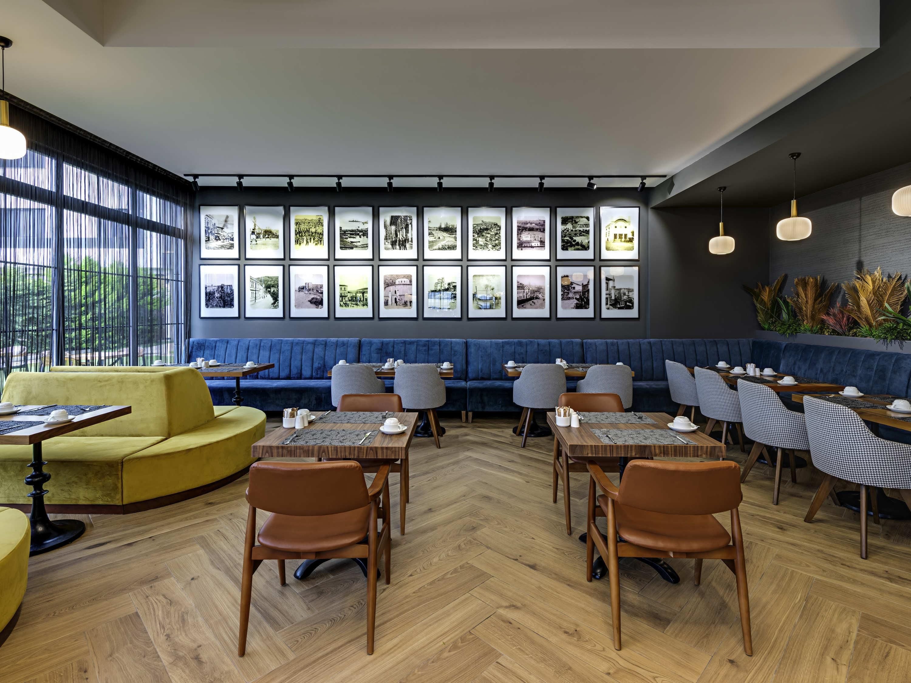 Un intérieur de restaurant moderne avec un plancher en bois, des sièges bleus et jaunes, et des tableaux encadrés accrochés au mur.