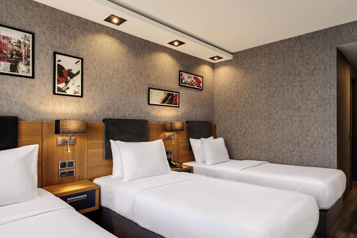 A hotel room with two beds, a wooden headboard, bedside lamps, a nightstand, and artwork on the walls.