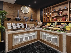 Montaje de bufé con diversos platos, una pared decorativa y un estante de madera con objetos.