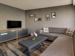 A modern living room with a flat-screen TV, grey sofa, wooden cabinet, and a coffee table with a vase of flowers. - Mövenpick Hotel Trabzon (Trabzon)