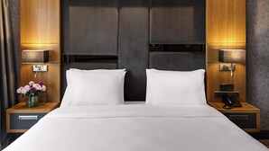 Una habitación de hotel moderna con una cama grande, cabecero de madera, lámparas de noche y una mesita de noche con un teléfono.