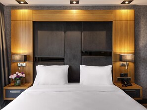 A modern hotel room with a large bed, wooden headboard, bedside lamps, and a nightstand with a phone. - Mövenpick Hotel Trabzon (Trabzon)