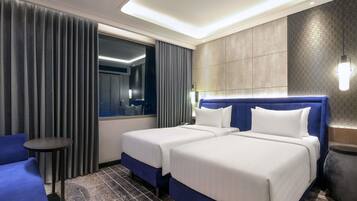 A hotel room with two beds, a blue chair, a small round table, and a large window with curtains.