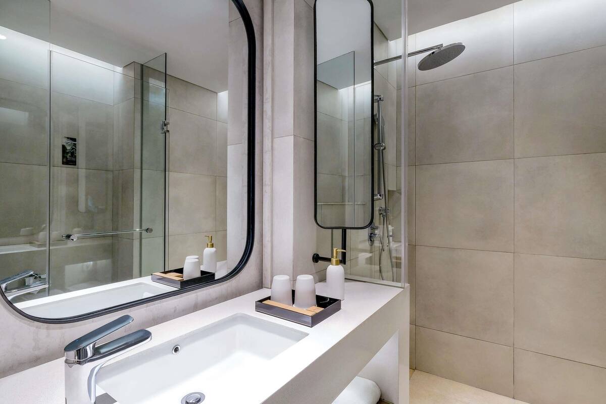 A modern bathroom with a large mirror, a sink, and a shower area.