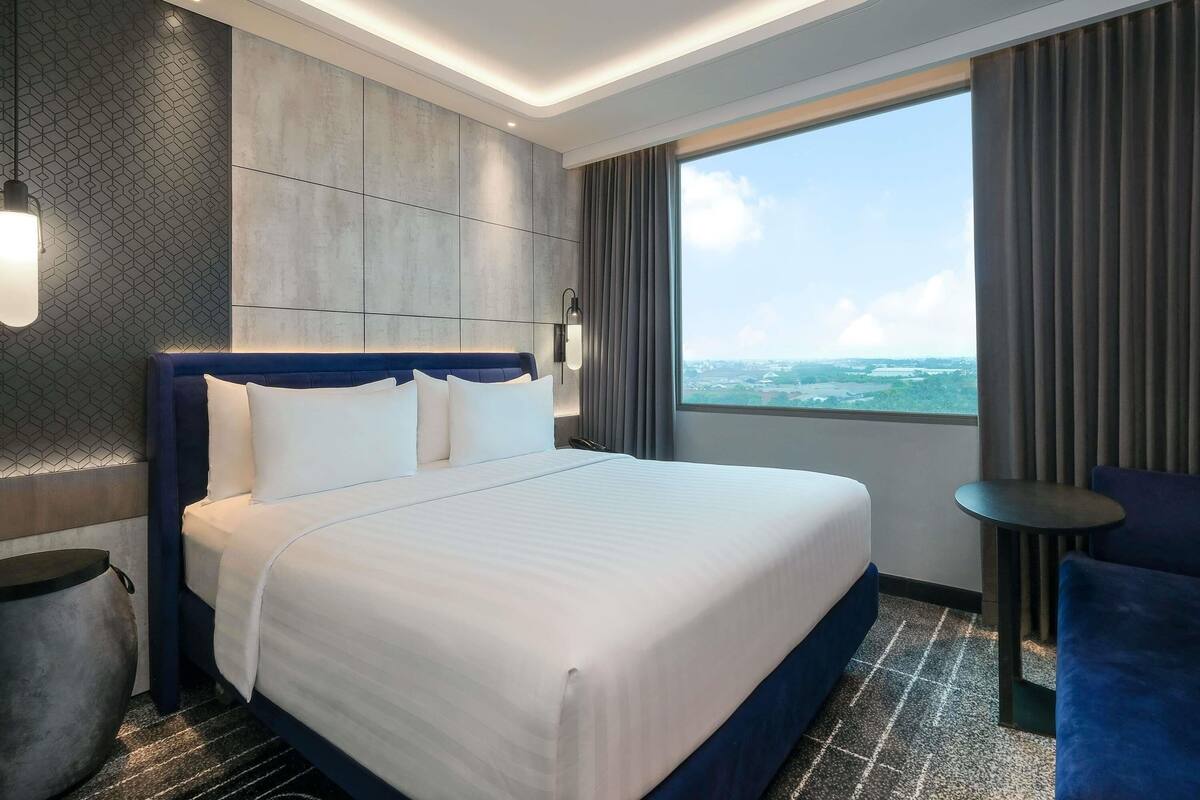 A modern hotel room with a large bed, a view of the sea, and a small table by the window.