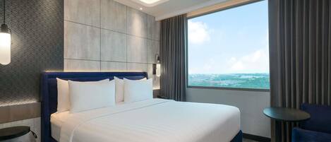 A modern hotel room with a large bed, a view of the sea, and a small table by the window.