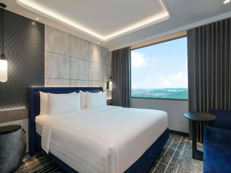 Una habitación de hotel moderna con una cama grande, vista al mar y una pequeña mesa junto a la ventana.