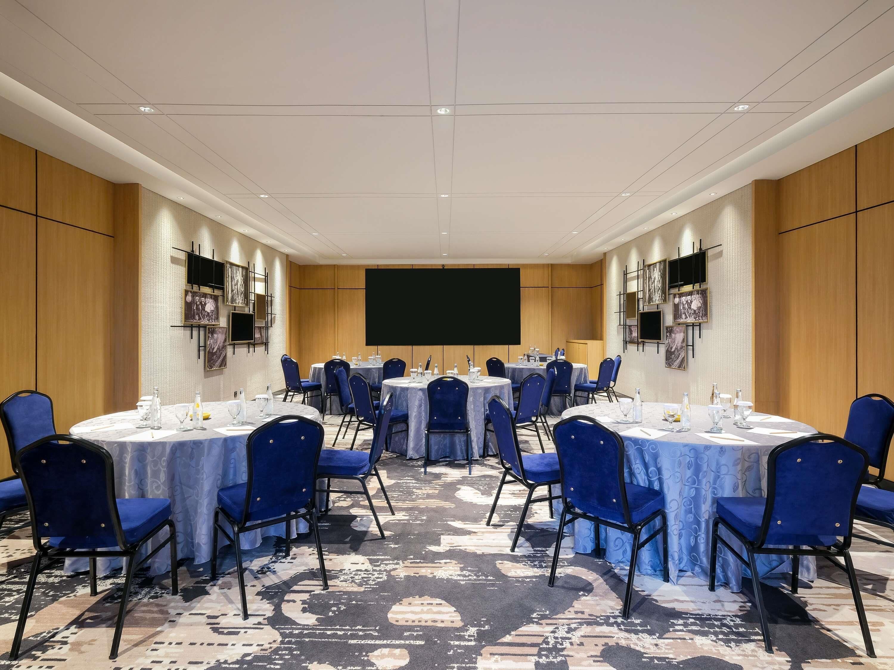 A conference room with round tables, blue chairs, and a large screen.