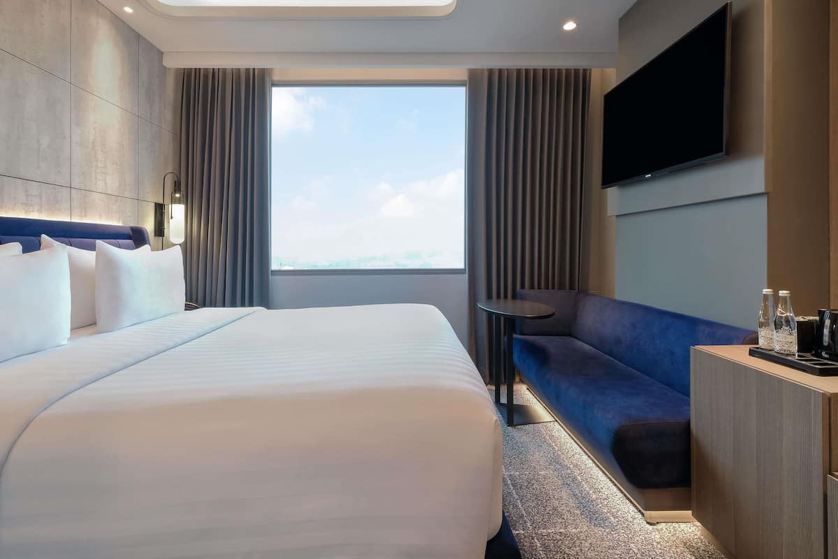 A hotel room with a large bed, a seating area, a flat-screen TV, and a view of the sky.