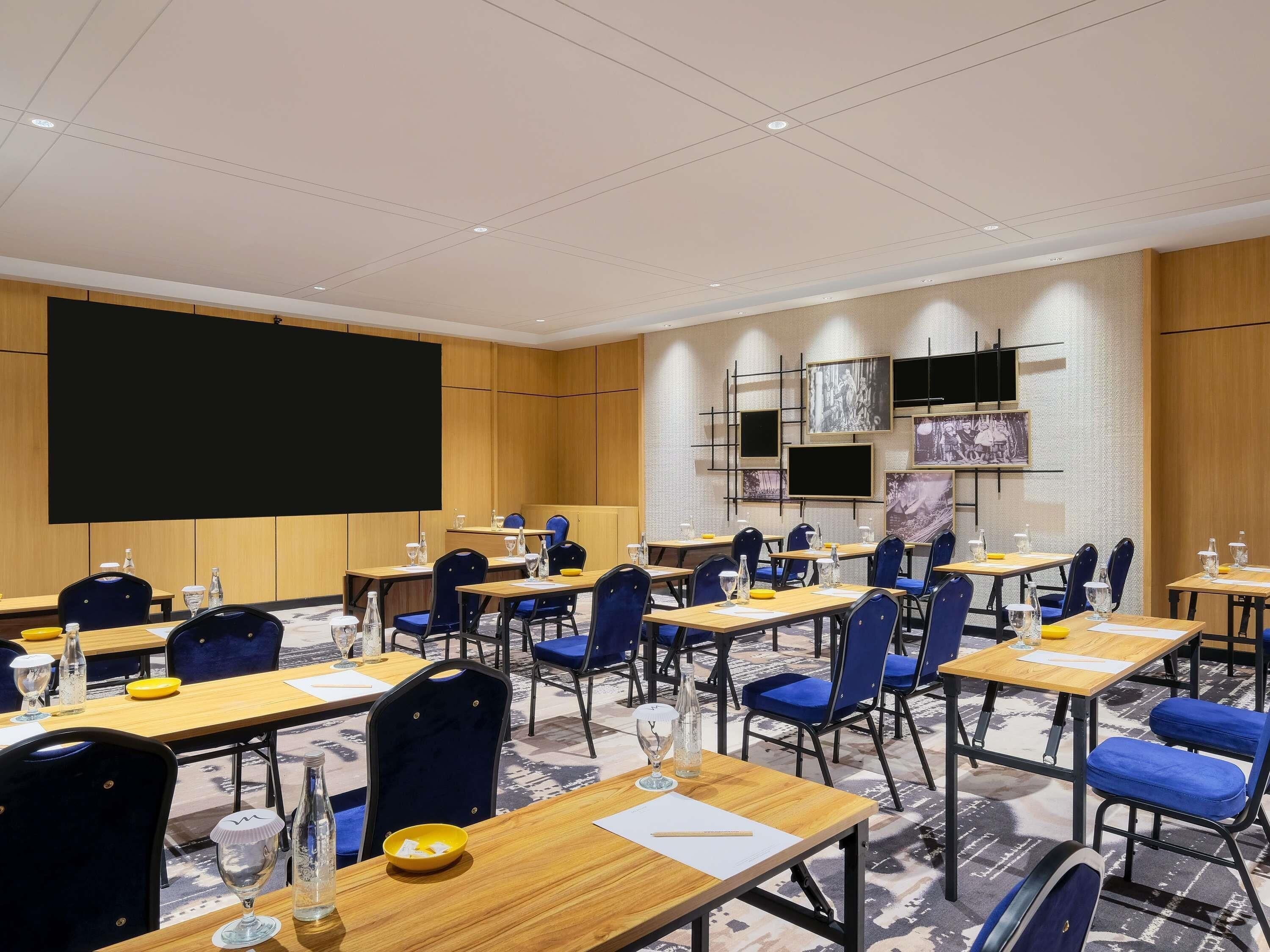 A conference room with multiple tables, chairs, a large screen, and a projector.