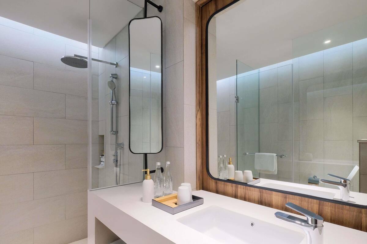 A modern bathroom with a large mirror, a shower, and a sink.