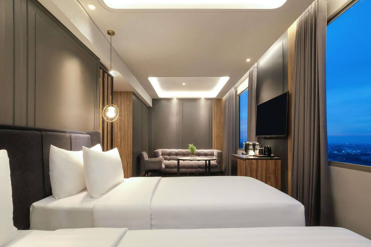 A hotel room with a large bed, a sofa, a coffee table, a TV, and a city view.