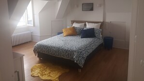 Un dormitorio con techo inclinado, una cama con ropa de cama estampada, una alfombra amarilla y una cita enmarcada en la pared.