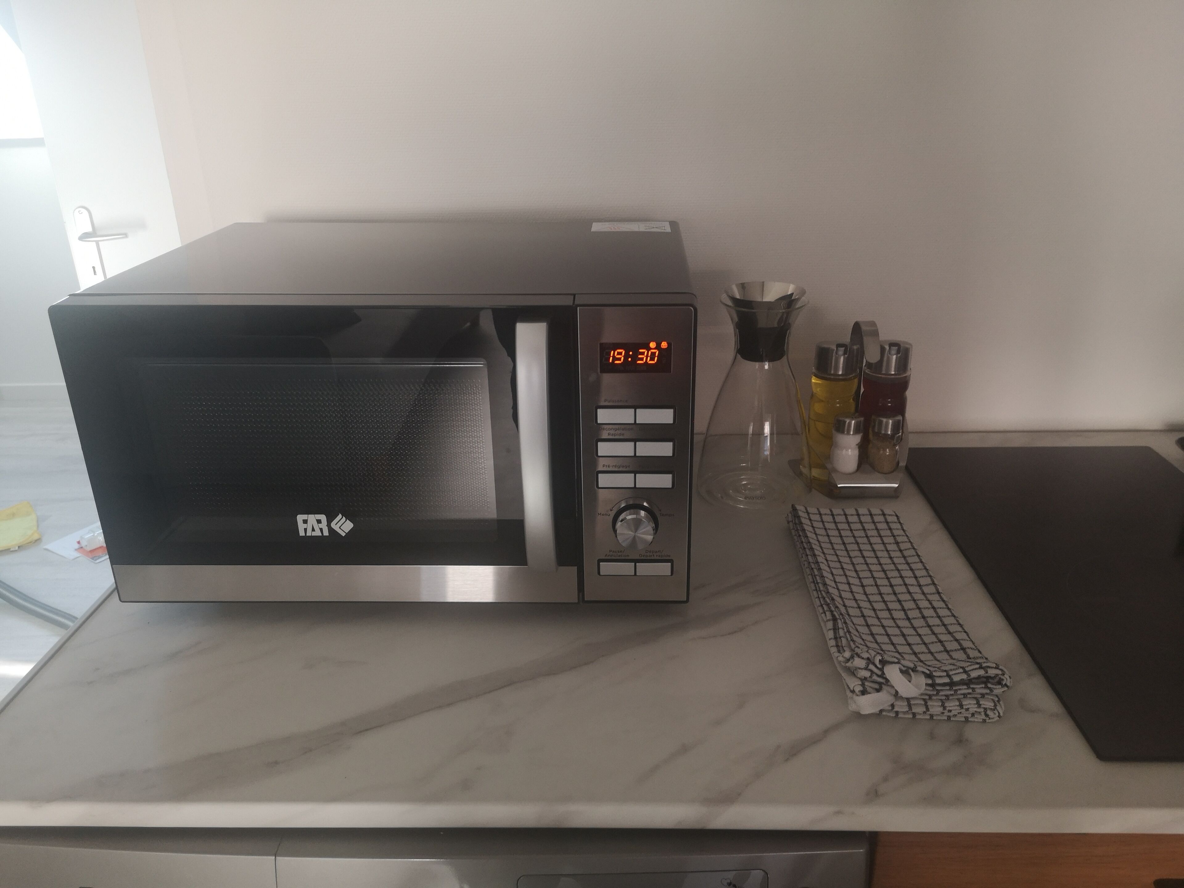 A modern kitchen with a stainless steel microwave, a coffee maker, and a kitchen scale on the countertop.