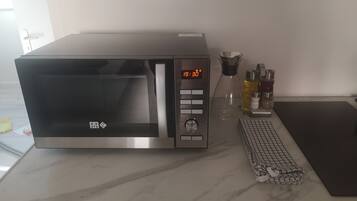 A modern kitchen with a stainless steel microwave, a coffee maker, and a kitchen scale on the countertop.
