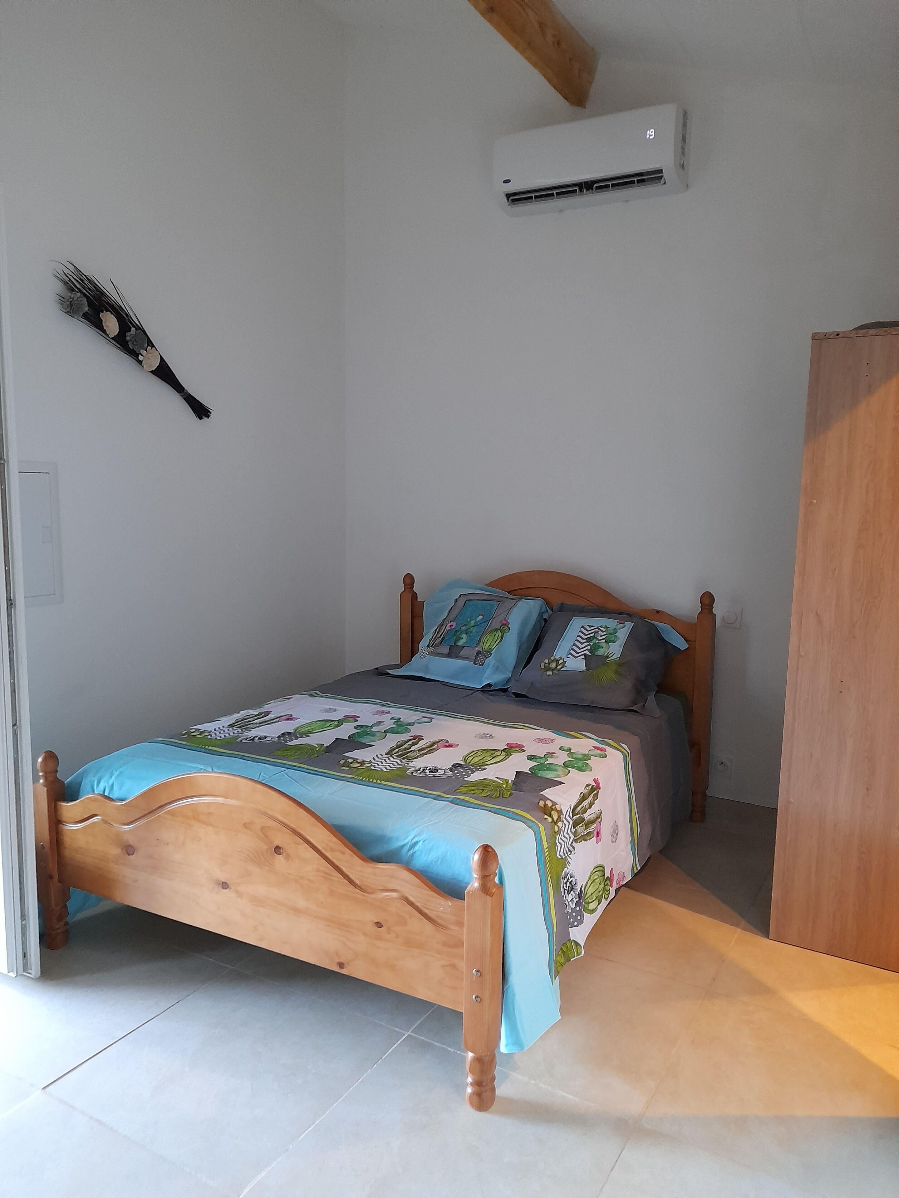 Een slaapkamer met een houten bed, een bedspreider met blauw- en groene patronen, en een kussen.