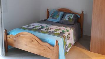 Een slaapkamer met een houten bed, een bedspreider met blauw- en groene patronen, en een kussen.