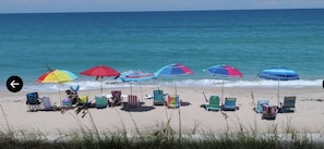 A beach with multiple colorful umbrellas and beach chairs lined up along the shore. - You can hear the waves (Melbourne Beach)