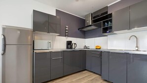 A modern kitchen with grey cabinets, a stainless steel refrigerator, a microwave, and a sink.