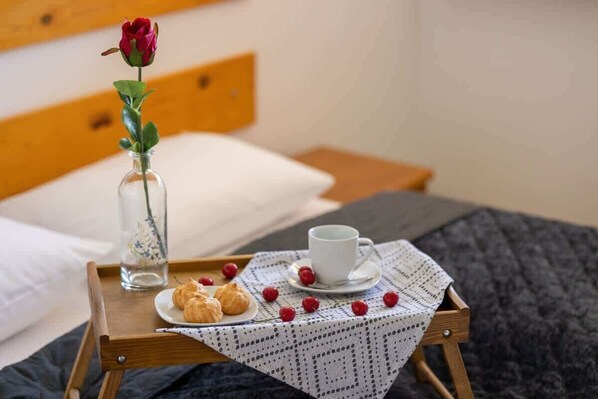 A wooden tray with a white lace tablecloth, a cup of coffee, a plate of croissants, a vase with a red rose, and a glass of water on a bed.
