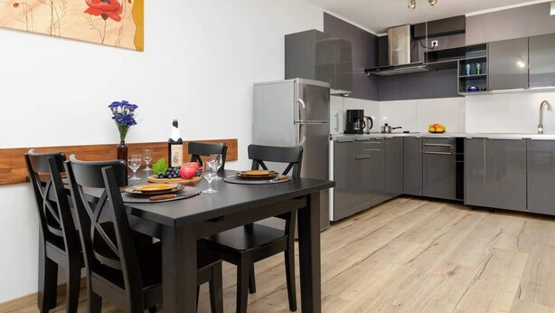 A modern kitchen with grey cabinets, a stainless steel refrigerator, and a dining area with a dark wooden table and chairs.