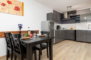 A modern kitchen with grey cabinets, a stainless steel refrigerator, and a dining area with a dark wooden table and chairs.