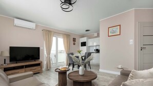 A modern living room with a flat-screen TV, sofa, coffee table, and dining area. - Apartment with Sea View | 200 m to the Beach, Balcony (Kolobrzeg)