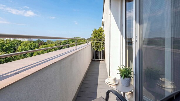 A balcony with a railing, a potted plant, and a table with a cup and saucer. - Apartment with Sea View | 200 m to the Beach, Balcony (Kolobrzeg)