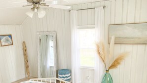 A bedroom with a large bed, wooden flooring, a ceiling fan, a window with curtains, and a vase with pampas grass. - Relaxing Coastal Inspired Cottage, short walk from the lake! (Ashtabula)