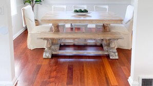 A dining area with a wooden table, white chairs, a chandelier, and a potted plant. - Relaxing Coastal Inspired Cottage, short walk from the lake! (Ashtabula)